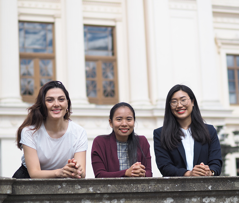 tree students in front of a white building. Photo. 